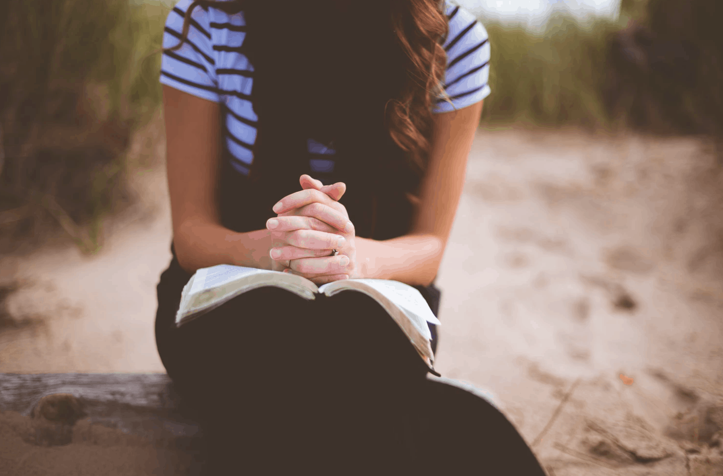 Healing From Church Hurt Woman in blue shirt with her head down and fingers laced in prayer over an open Bible